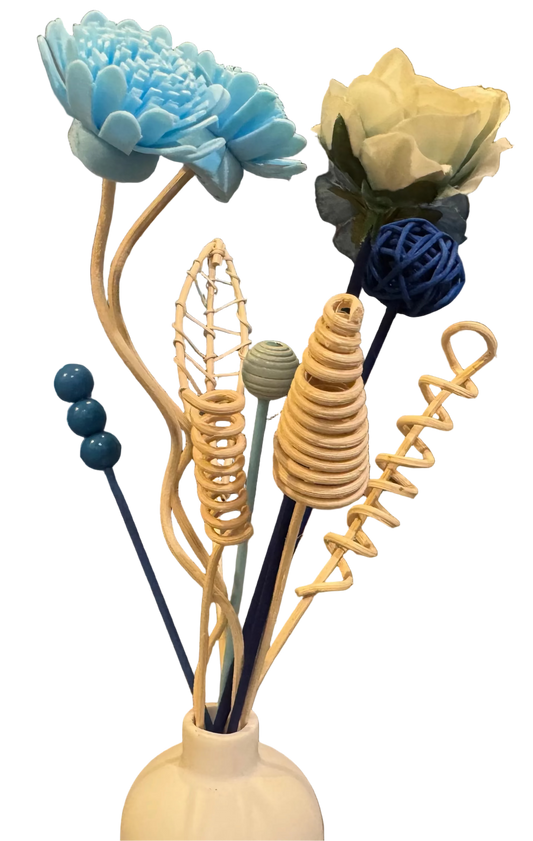 Decorative reed diffuser flower arrangement with blue, white, and beige flowers in a white vase on a table.