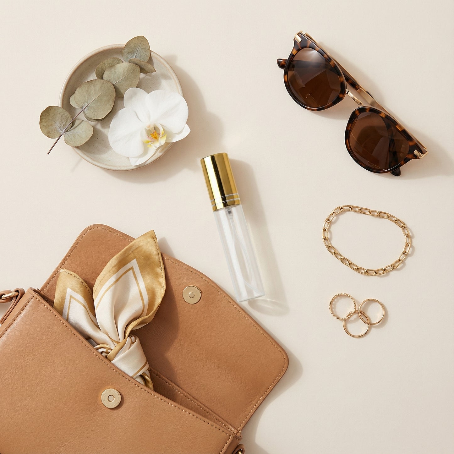 Tan handbag with scarf, perfume bottle, sunglasses, and jewelry on a light background